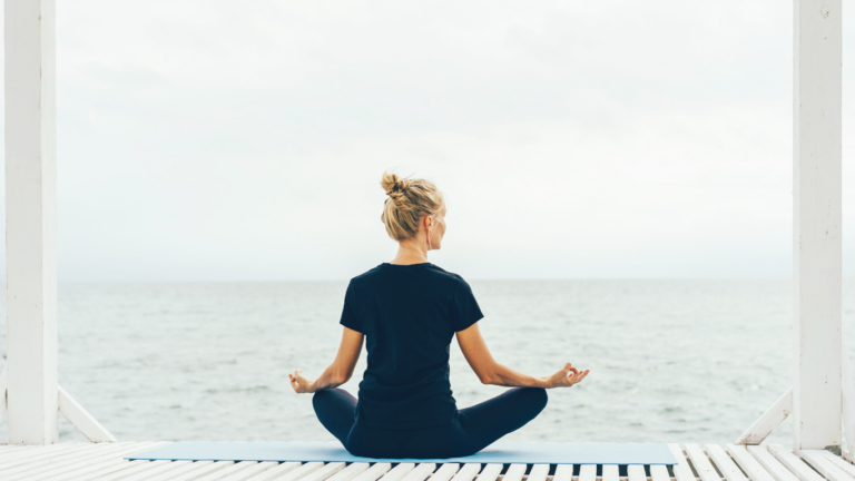 Woman mediataing in front of ocean representing a safe space.