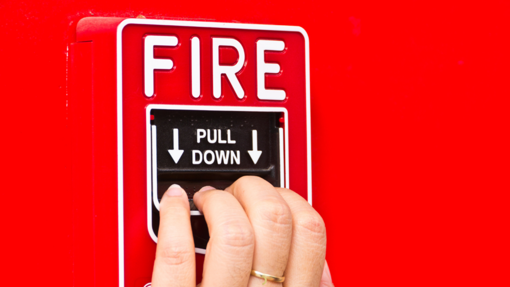 A red fire alarm with fingers ready to pull it down signifying the fact that chronic pain is a false alarm. This simplifies the healing process.